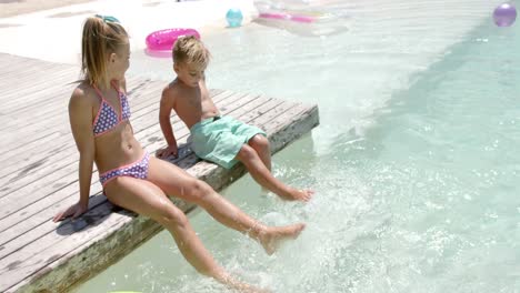 happy caucasian siblings playing at swimming pool with inflatables