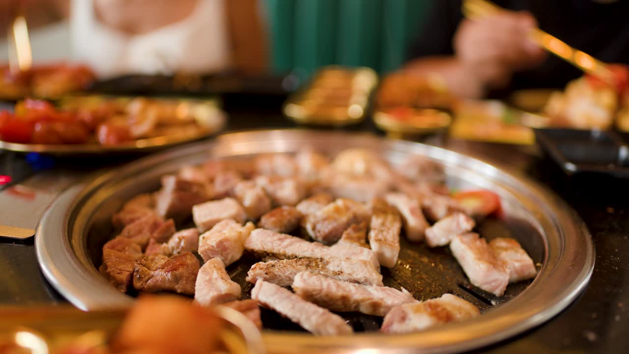 Sizzling pork belly cooks on a round grill, steam rising in a warmly lit restaurant