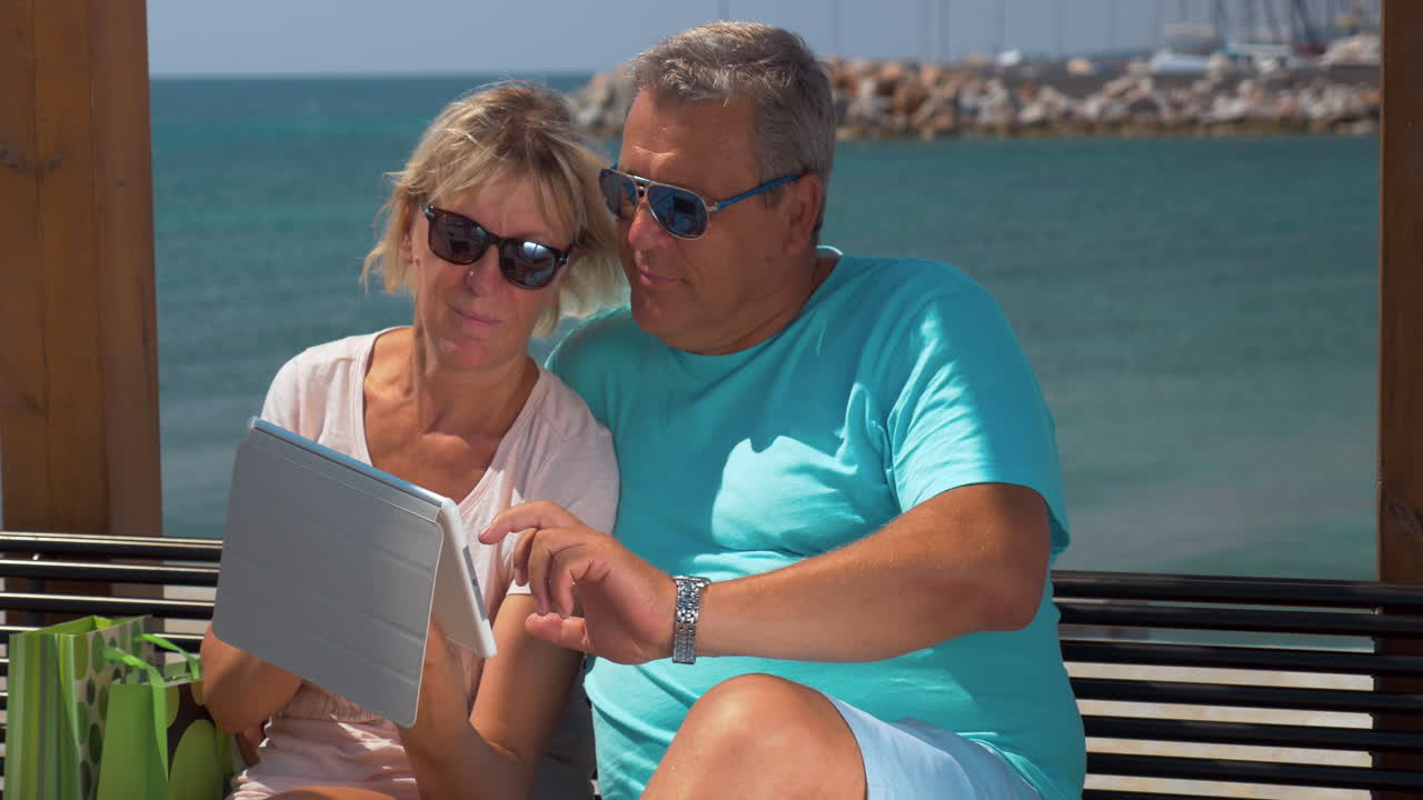 Pareja mayor usando una tableta en el paseo marítimo