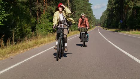 two people cycling on a road through a forest