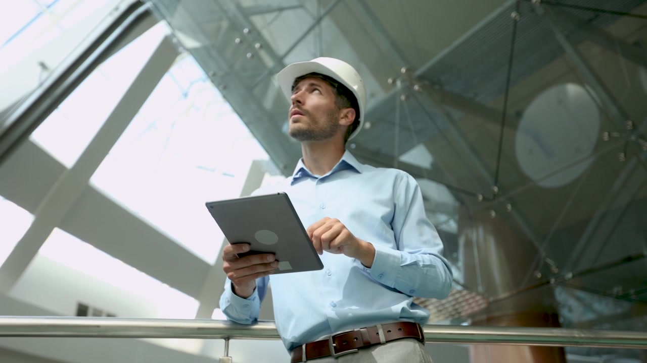 Engineer in Hard Hat Using Tablet and Looking Up in Modern Building