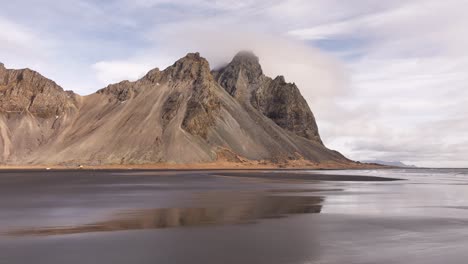 still shot of vestrahorn mirrored on black sand beach after receding tide. stokksnes, iceland