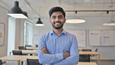 young manager posing with crossed arms and a confident smile in a spacious, bright office, embodying professionalism and success in a modern workplace environment