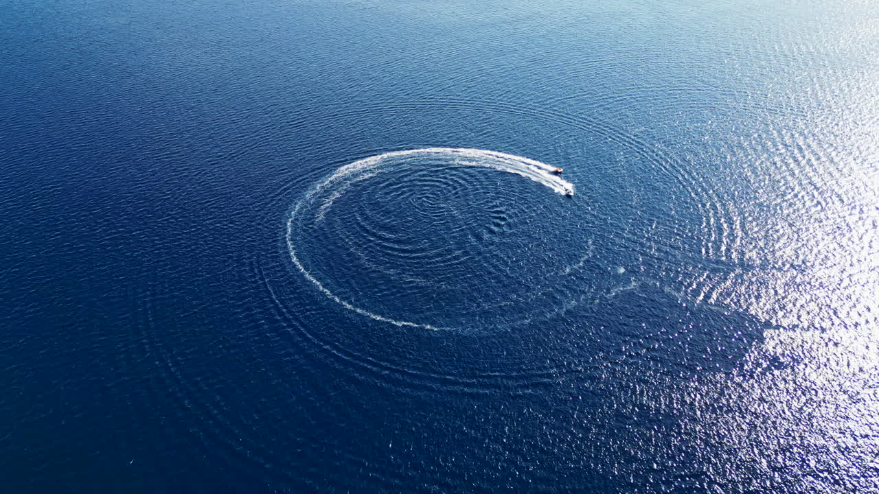 White motorboat cruising on rippled blue water, leaving a circular wake. Drone flying forward. Croatia