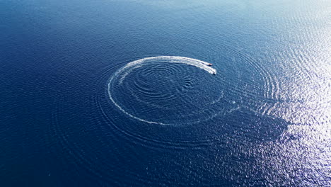 white motorboat cruising on rippled blue water, leaving a circular wake. drone flying forward. croatia