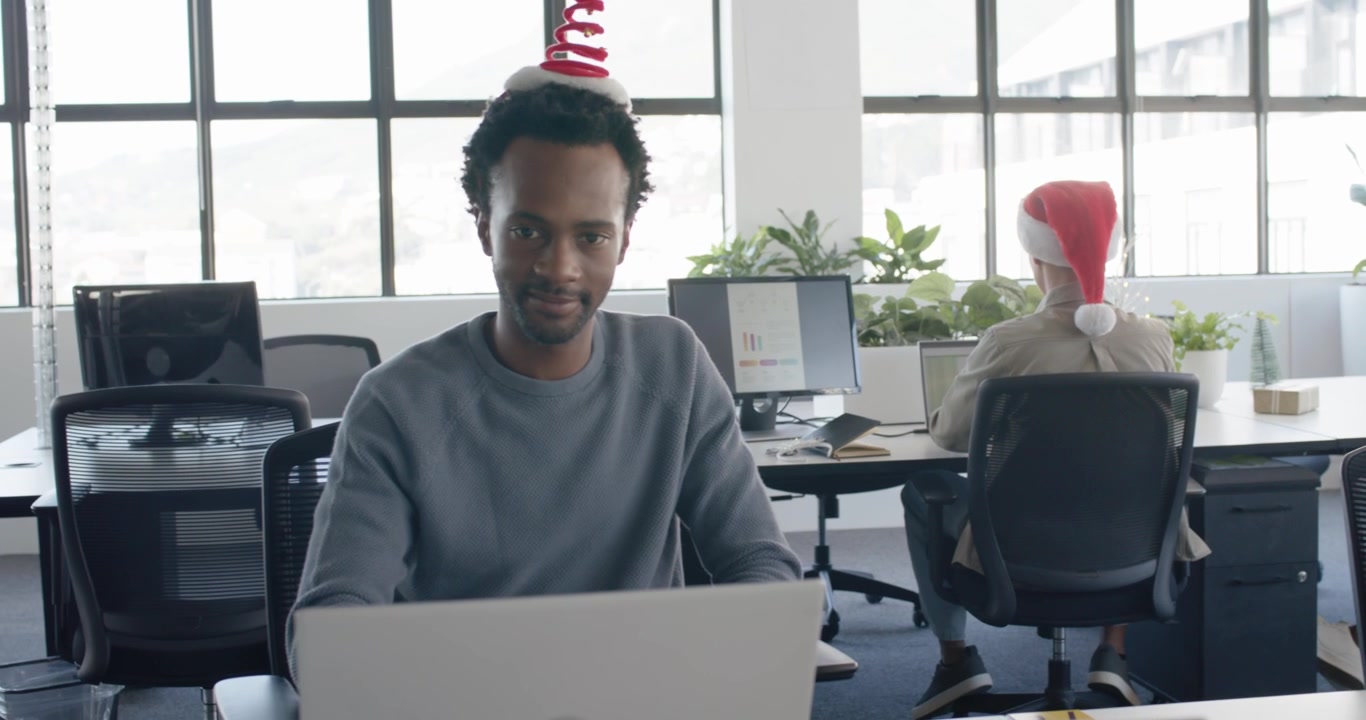 Christmas cheer inspiring African-American man typing laptop at desk pal scrolling phone