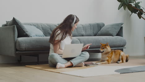 pretty girl feeds and pets her dog while working on her laptop at home