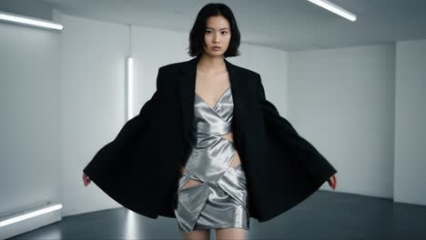 a fashion model showcasing an elegant silver dress with tailored blazer in a minimalistic studio setting, highlighting modern style and sophistication