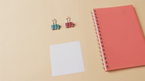 close up of red notebook and school stationery arranged on beige background, in slow motion