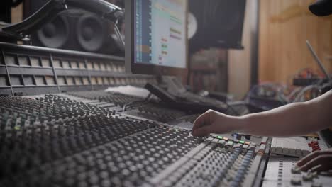 sound producer is looking on a display of a digital audio workstation in a sound engineer room and rotating handles