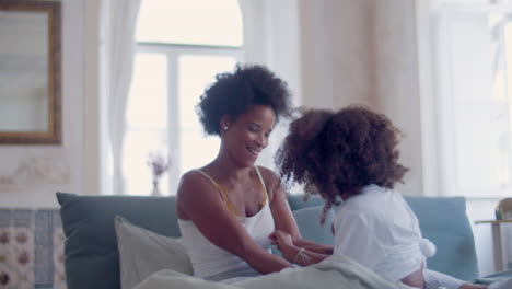 cheerful african american mum and daughter tickling each other in bed, laughing and having fun together