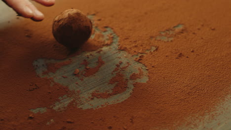 closeup chef hand rolling chocolate truffle in cocoa powder in slow motion.