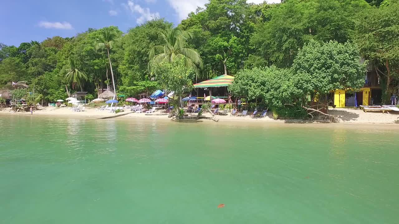 toma aérea al revés de una pequeña playa con restaurantes y bungalows en koh chang que revela vistas a la jungla y al mar