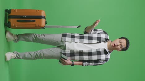 full body of wondering asian male traveler with luggage holding passport and standing doubtfully in the green screen background studio