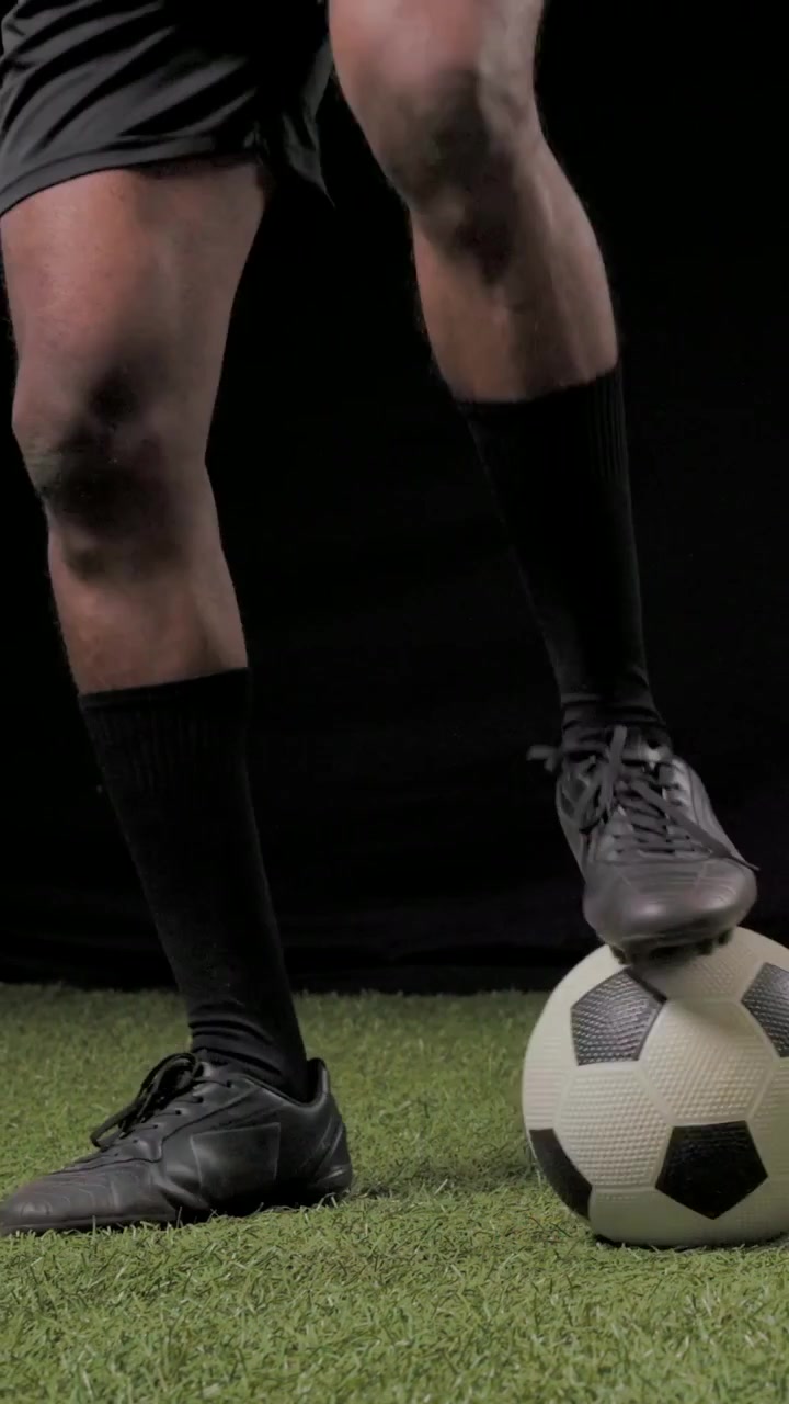 Dikey video: Top yuvarlanıyor, kramponlu oyuncu stüdyo çiminde antrenman için futbol topunu kontrol ediyor.