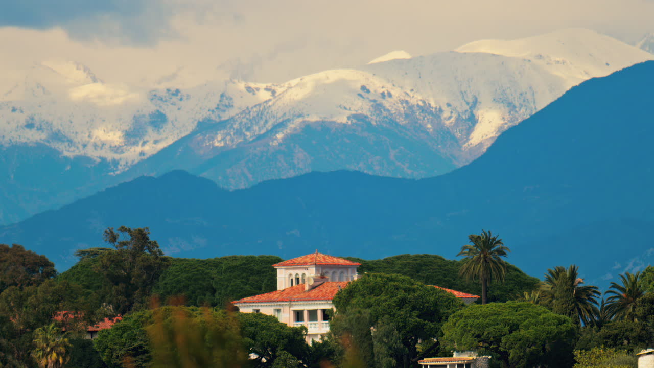 Distant view of orange villas surrounded by green trees with the mountains on the background on a cloudy day