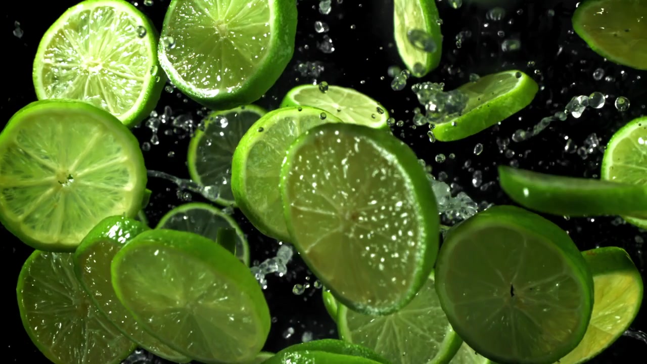 Fette di lime verde fresco che cadono al rallentatore con schizzi d'acqua