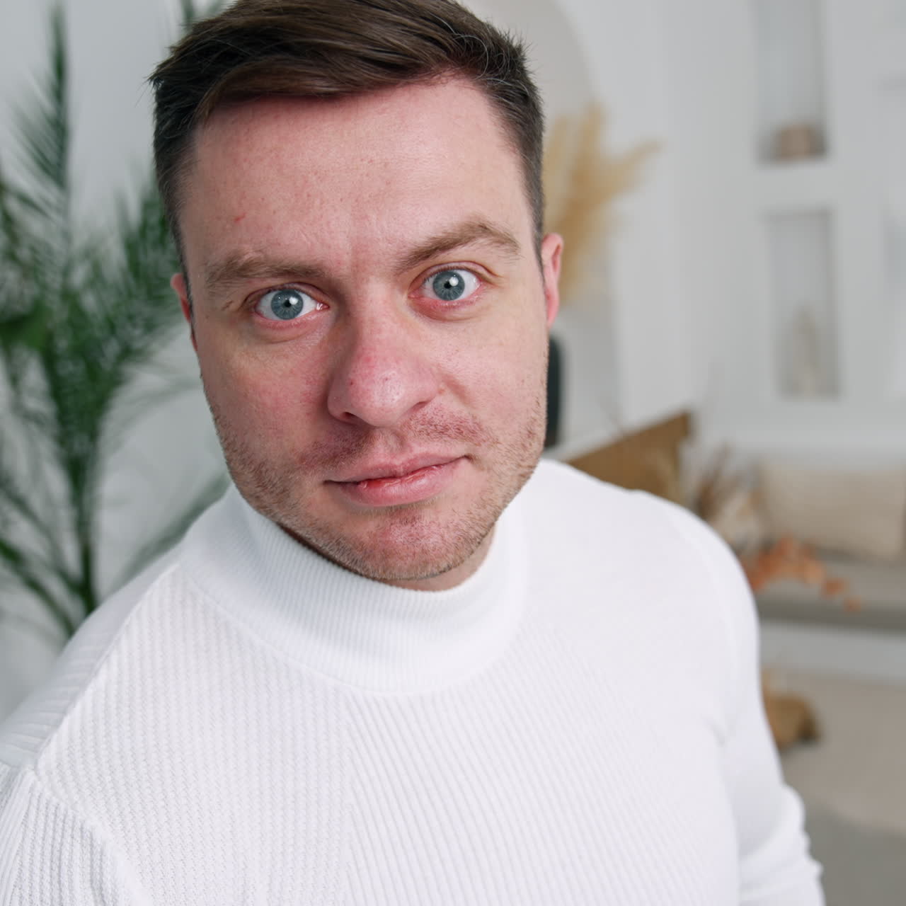 Caucasian male wearing white sweater standing near the camera. Cropped image of a man in the room. Close up.