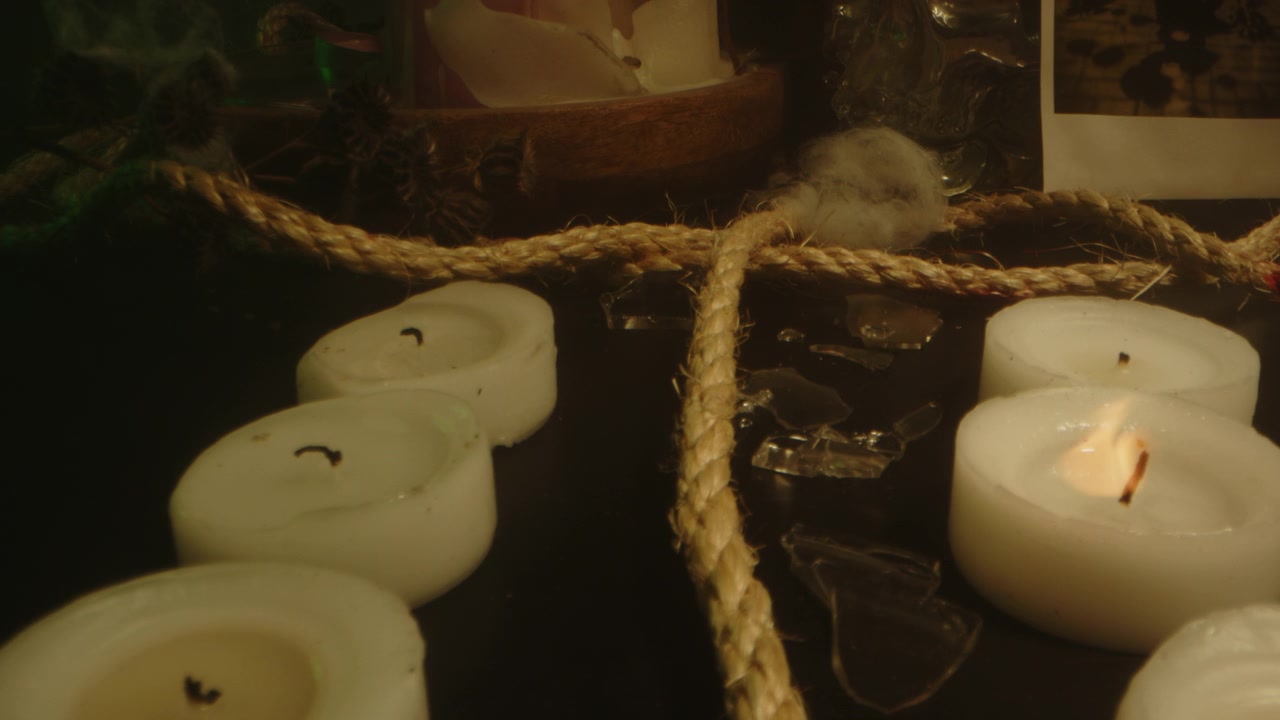 Eerie macro dolly in of a long rope running to an occult altar in a room filled with smoke and burning candles