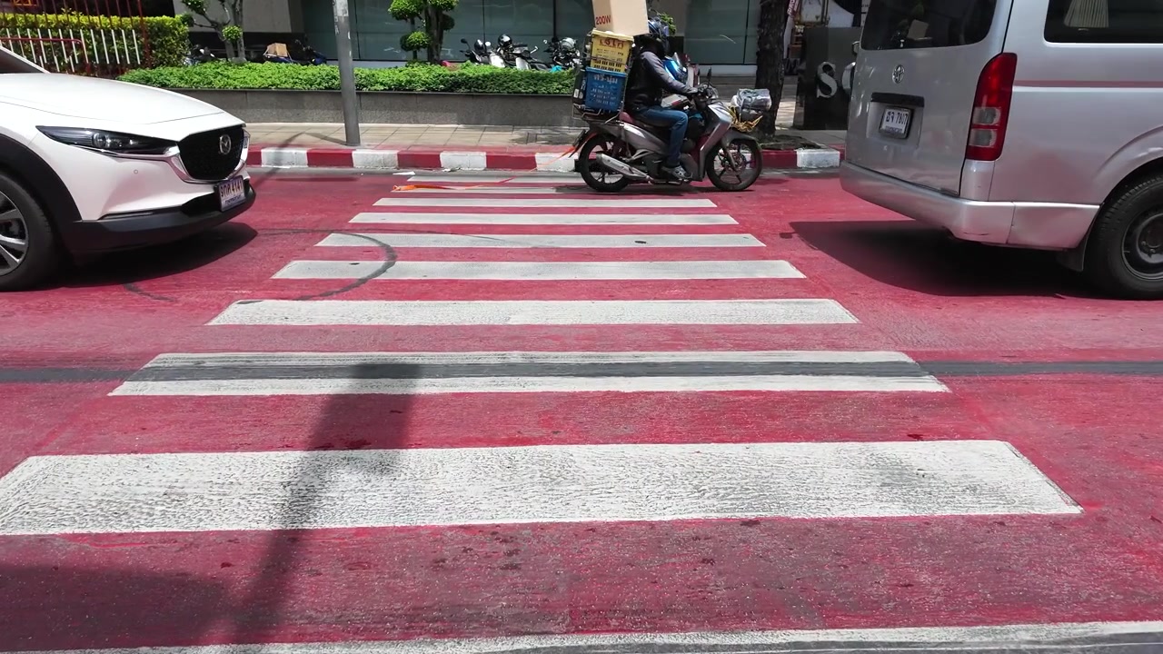 Static wide shot of vehicles passing over a vibrant red pedestrian crosswalk in Bangkok, Thailand.