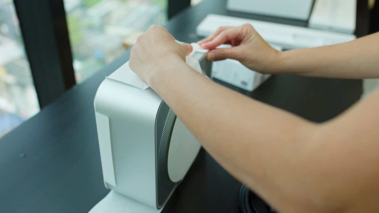 Hands carefully unbox and unwrap a compact desktop computer on a modern office desk