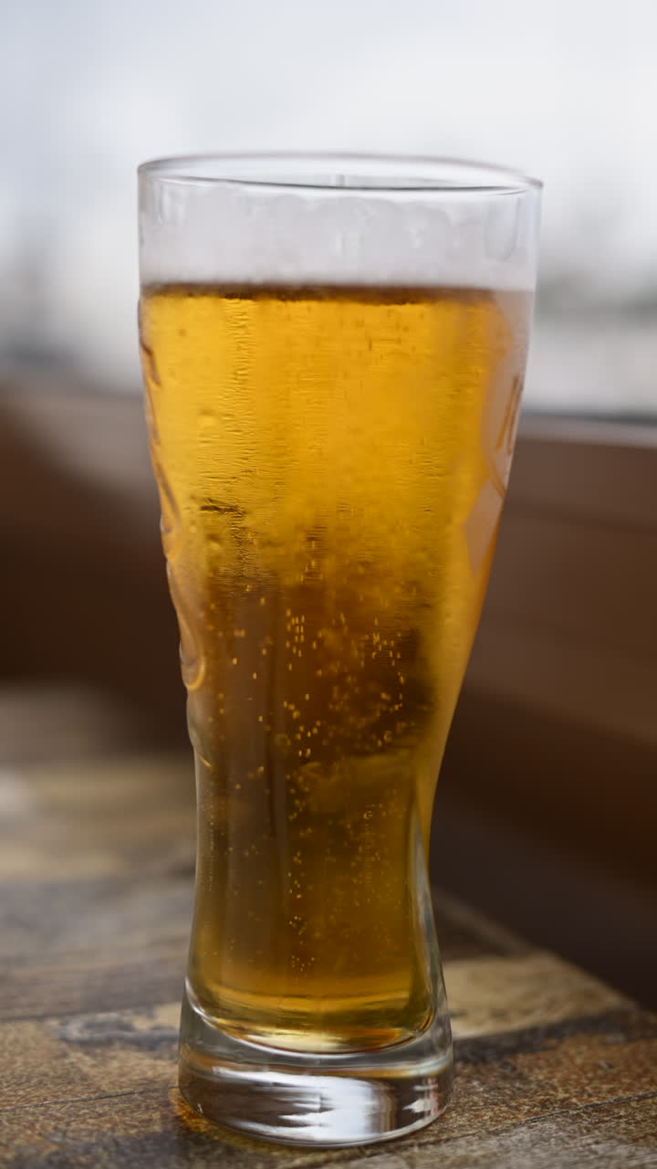 Primo piano di un bicchiere freddo di birra dorata con bollicine e schiuma visibili. Verticale