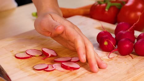 cortando a mano rábanos con tomates y zanahorias cerca