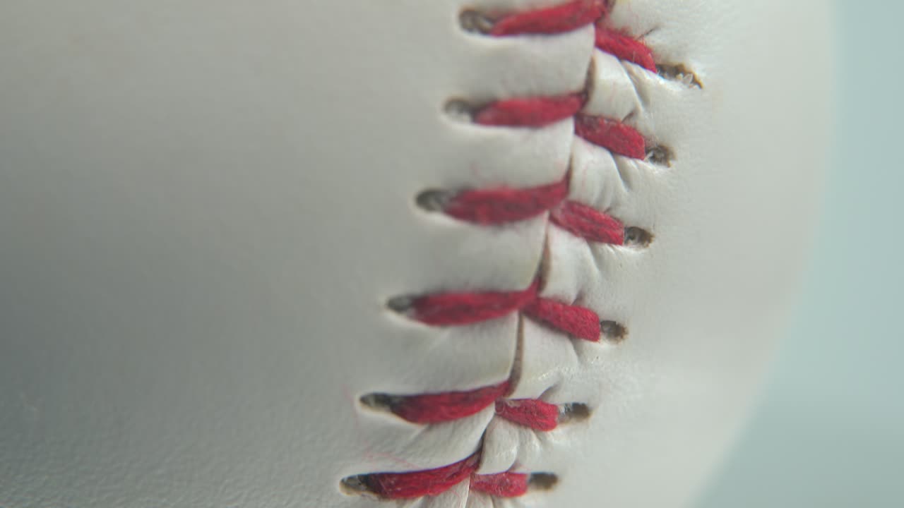 Macro inquadratura cinematografica di una palla da baseball bianca, primo piano sulle cuciture rosse, palla da baseball su un piedistallo lucido, luce professionale da studio, video 4K con tilt up.