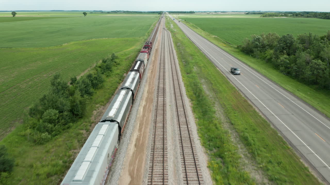 vista aérea del viaje del tren de carga a través del campo rural con la carretera adyacente