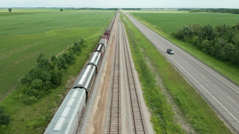 Aerial-View-of-Cargo-Train-Journey-Through-Rural-Countryside-with-Adjacent-Road