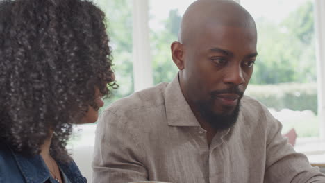 couple sitting around table at home shopping or booking holiday on laptop