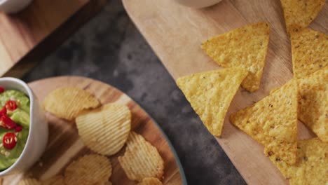 Close-up-view-of-variety-of-chips-and-sauces-on-wooden-trays-on-black-surface