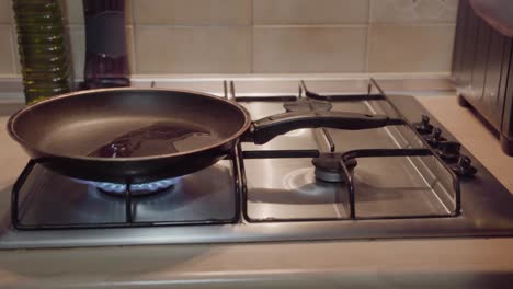 pouring baking oil on frying pan in kitchen on gas stove, smooth it out after