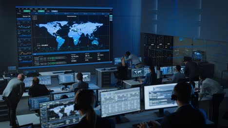 tomada estática de oficiales en un centro de control de vigilancia con el seguimiento del mapa global de la policía en una gran pantalla digital. los empleados de la sala de monitoreo se sientan frente a pantallas de computadora y analizan grandes datos.
