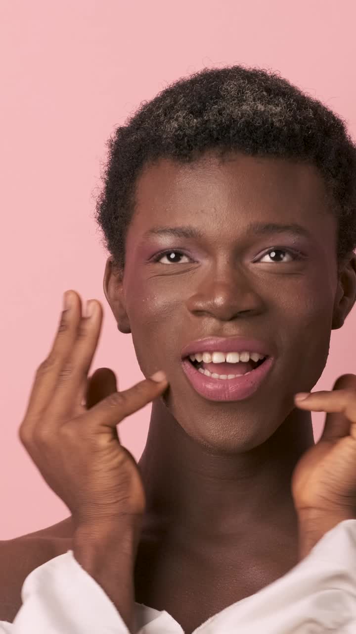 Glückliche, sanfte Transgender-Person berührt im Studio die Wangen. Vertikalaufnahme.