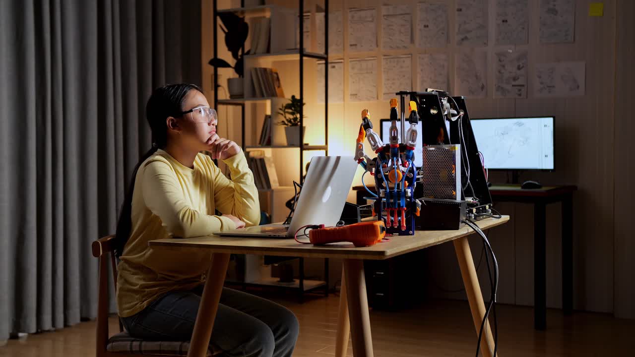 십대 아시아 소녀가 집에서 노트북에 사이보그 손을 는 동안 생각하고 있습니다.