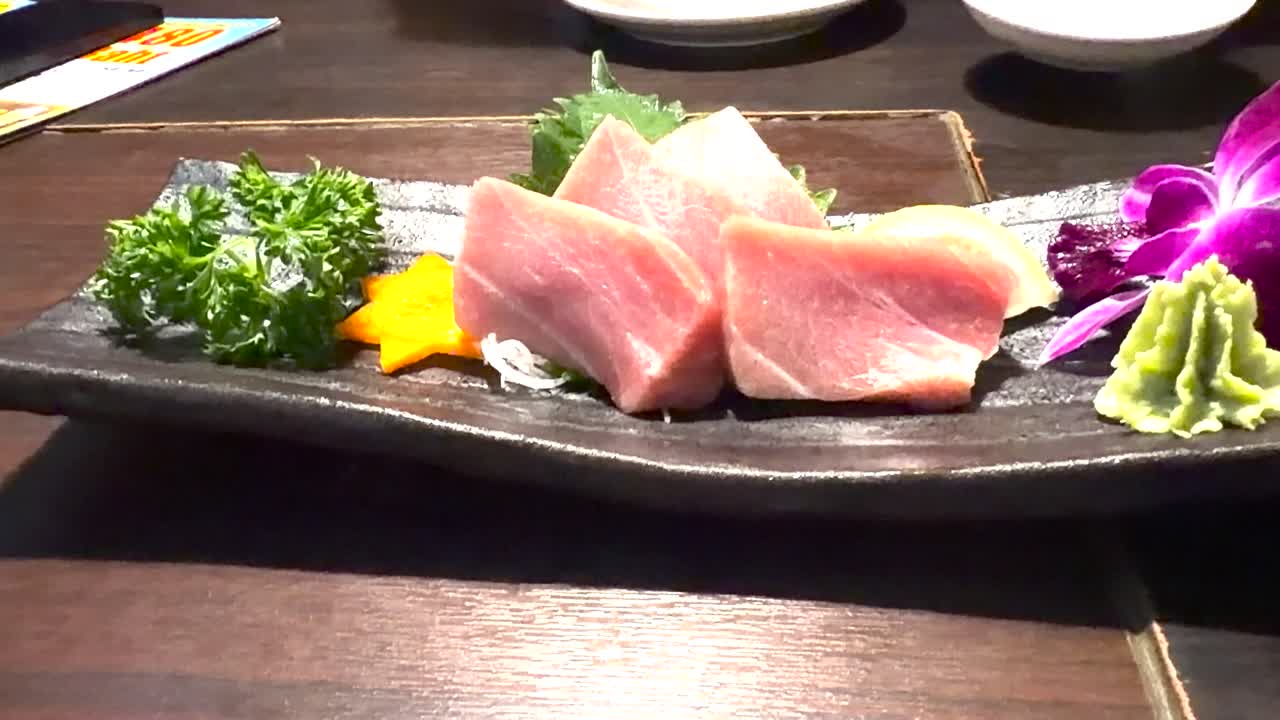 Hand uses chopsticks to pick up fatty tuna sashimi on elegant restaurant platter