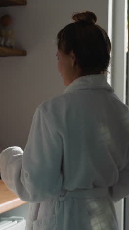 una mujer hace una bebida con una cafetera en la cocina. una dama con una bata de baño suave viene a la máquina de café preparando una bebida aromática. el concepto de una mañana relajada