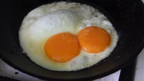 hot fried egg preparation on old cast frying pan for breakfast