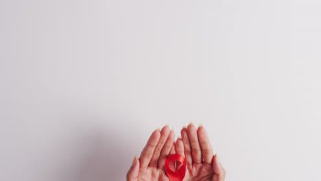 Video-of-hands-of-caucasian-woman-holding-red-ribbon-on-white-background