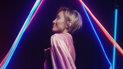 side view of cheerful blonde woman in extraordinary style dancing and moving on neon wall with colorful lamps