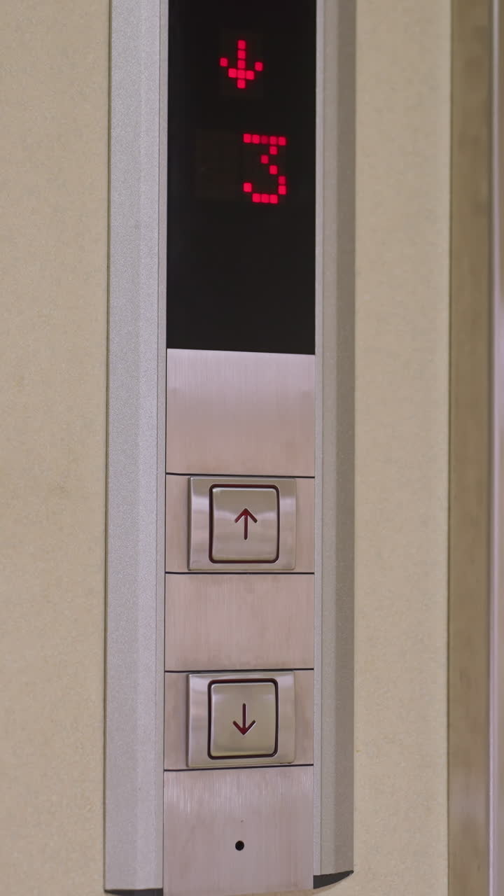 Elevator control panel showing floor number indicator with red digits and up down buttons. Modern metal design with clear display showing floor 3, indicating movement or selection in office building