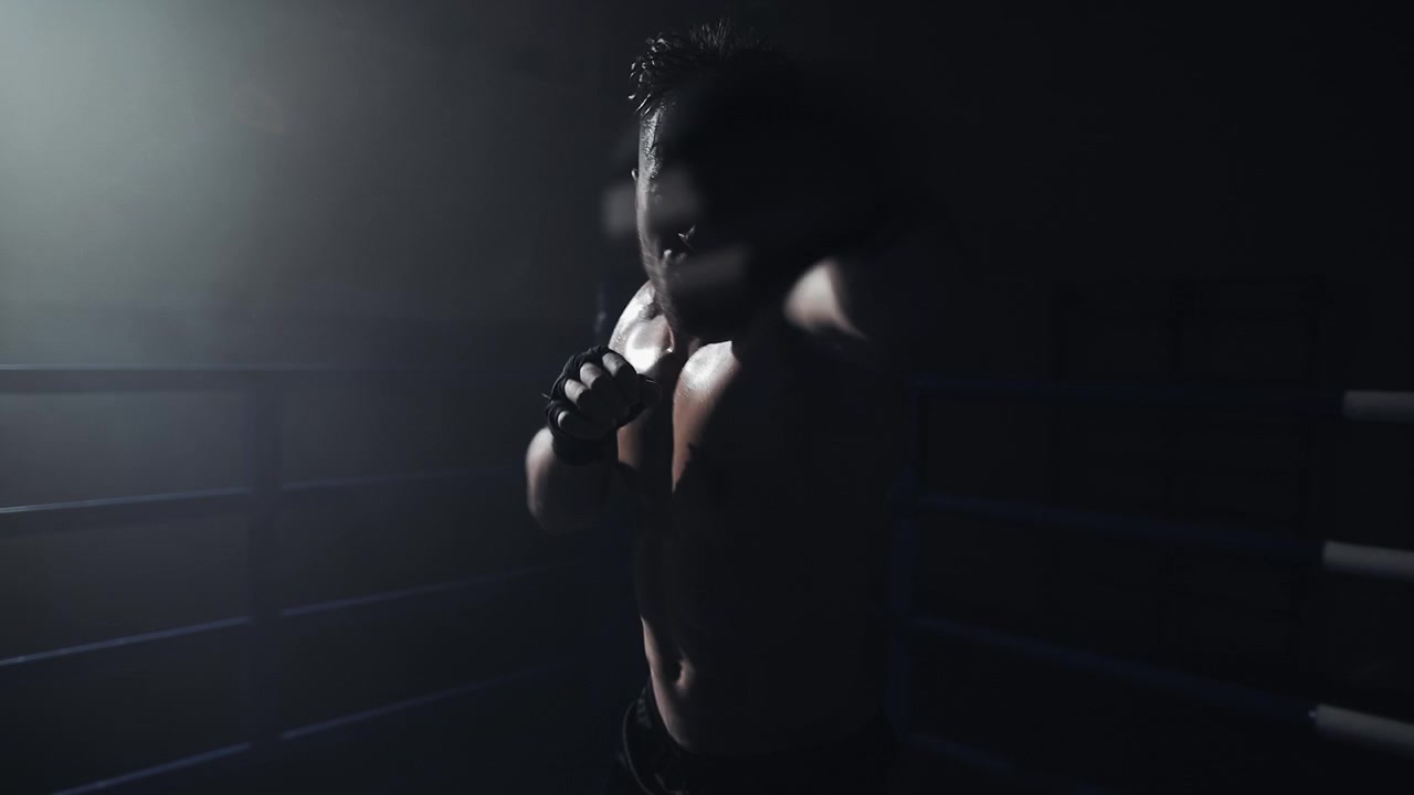 Intense Boxer Shadow Boxing in a Dark, Backlit Ring