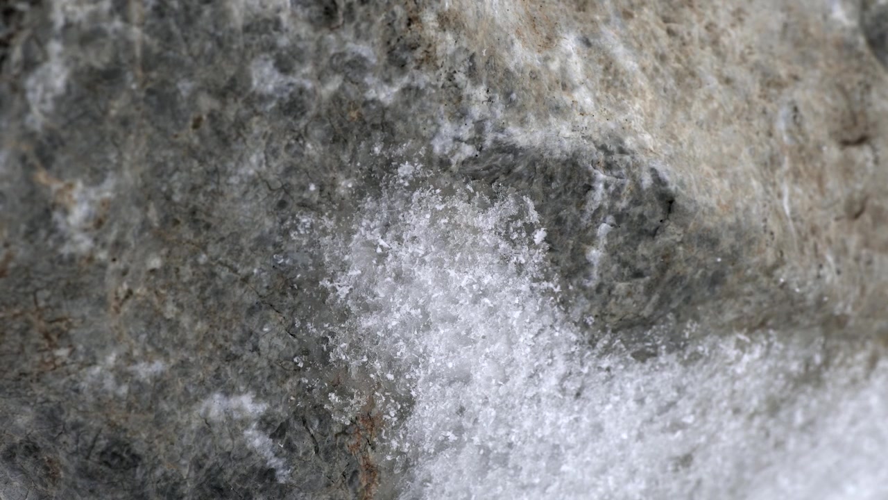 Close-up van smeltende sneeuw op een gestructureerd rotsoppervlak
