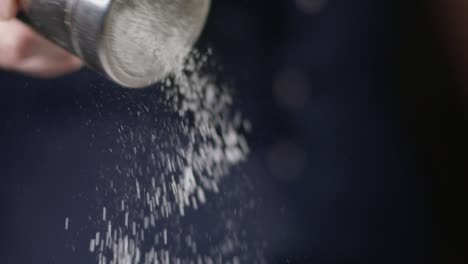 person sifting white powder with metal shaker while preparing dish