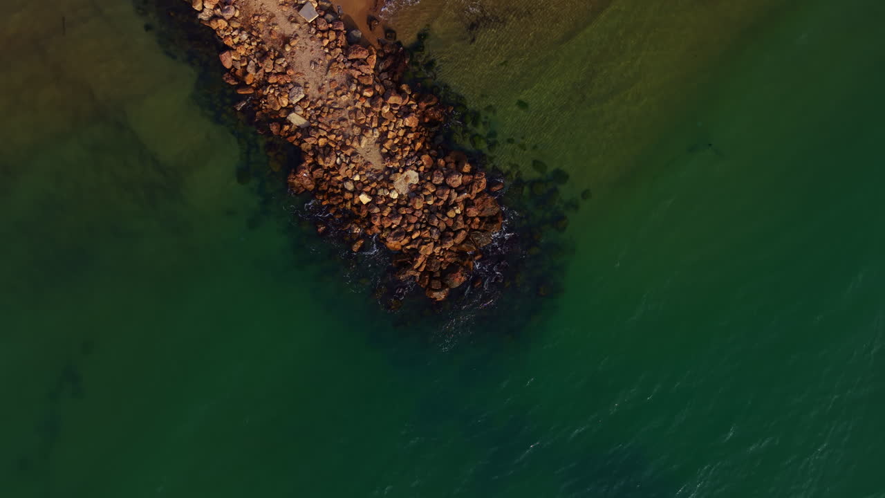 Bølgerne slår blidt mod den stenede mole på en rolig eftermiddag ved den fredfyldte strand.