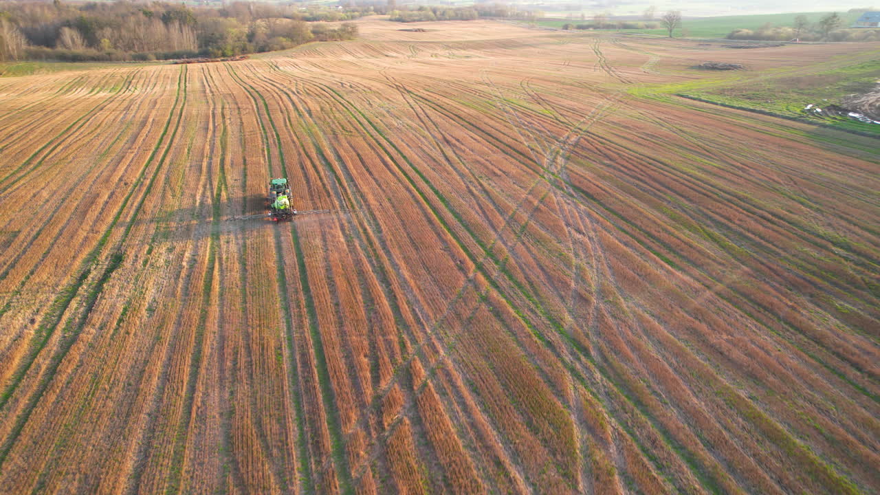 Aerial arc tracking shot above farm land of green sprayer tractor spraying crops