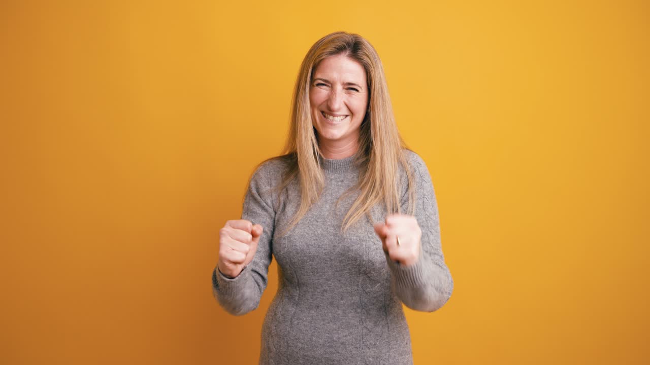 Donna felice che celebra il successo con i pugni in aria su sfondo giallo