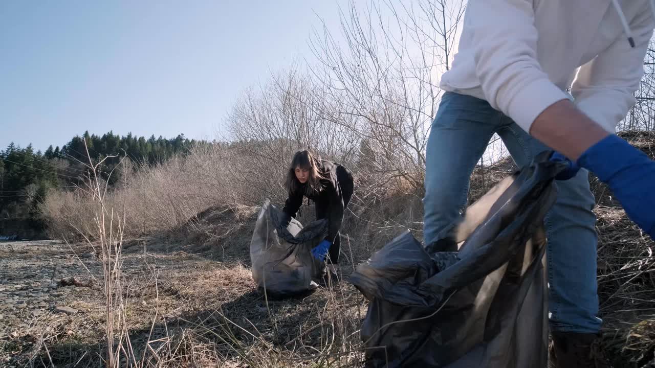Teamwork cleaning plastic on the beach. Volunteers collect trash in a trash bag. Plastic pollution and environmental problem concept. Voluntary cleaning of nature from plastic. Greening the planet