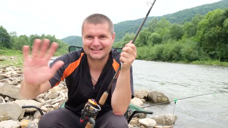 portrait of a handsome contented young fisherman with a fishing rod sitting near a mountain river portrait of a handsome contented young fisherman with a fishing rod sitting near a mountain river fishing in the middle of a beautiful mountain landscape